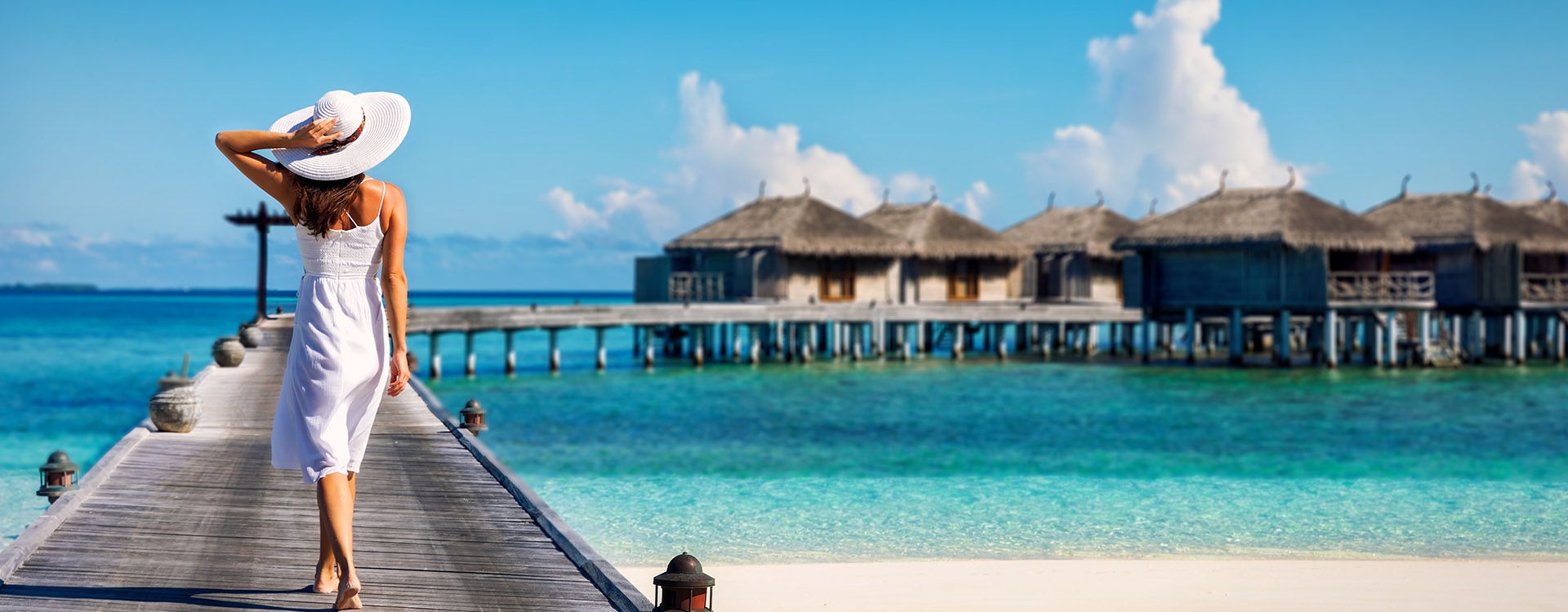 Woman in white walking over a wooden jetty in the Maldives