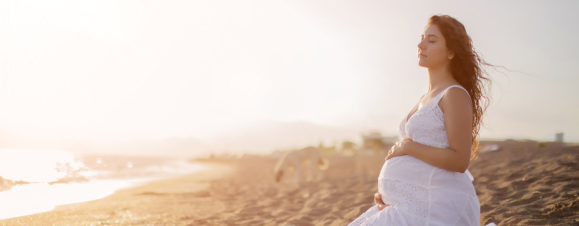 Young beautiful pregnant woman on the beach. Relax by the calm sea in sunshine