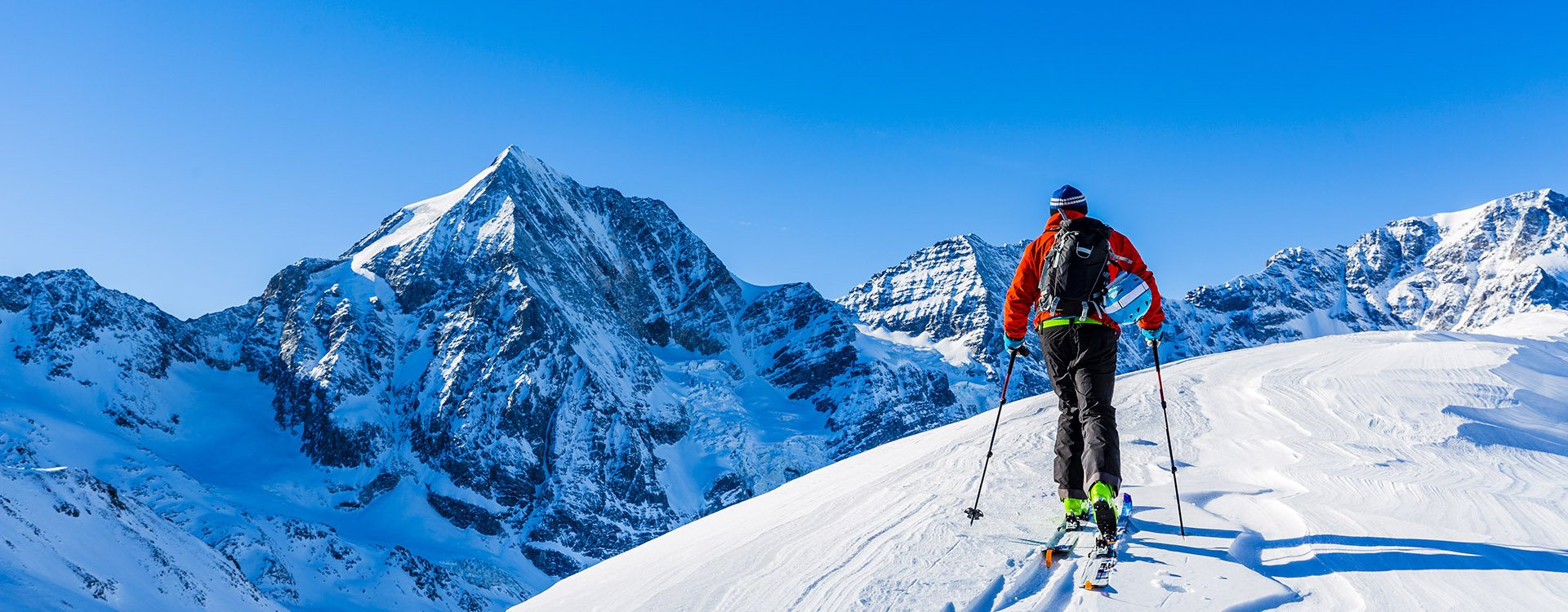 Mountaineer backcountry ski walking up along a snowy ridge with skis in the backpack.