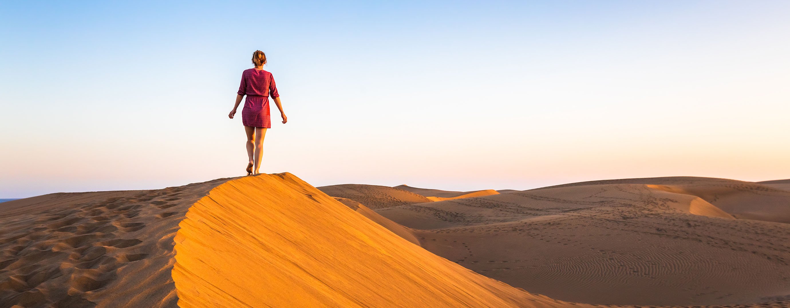 Girl walking on sand dunes in arid desert at sunset and wearing dress, scenic landscape of Sahara or Middle East
