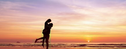 Couple kissing on the beach with a beautiful sunset in background