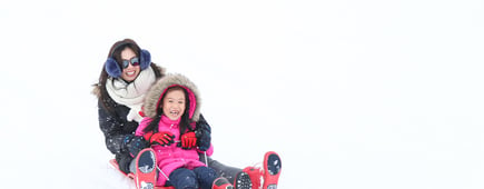 Cute Asian little girl plays sled with her mother in the white and fluffy snow hill in the ski area in Japan