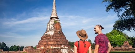 Young Couple in red clothes with photo camera looking at ancient ruined Wat Mahathat in Ayutthaya, Thailand