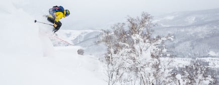 Backcountry skier jumps off a cornice in Hokkaido, Japan. Yellow jacket, blue backpack
