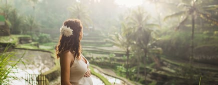 Young pregnant woman in white dress with view of Bali rice terraces in morning sunlight. View from behind. Harmony with nature