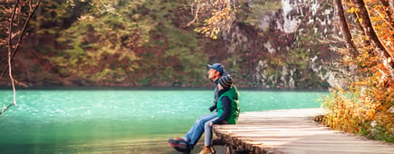 Weekend in autumn park: father with son sit on bridge near the mountain lake