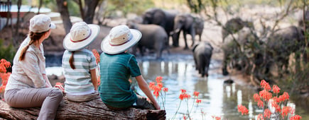 Family of mother and kids on African safari vacation enjoying wildlife viewing at watering hole