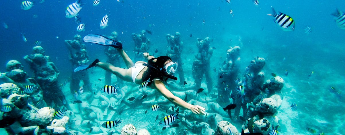 Snorkel woman swimming in a turquoise ocean under the flooded statues. Free diving.