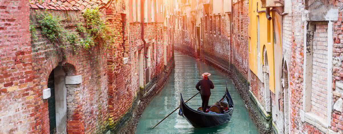 Venetian gondolier punting gondola through green canal waters of Venice Italy
