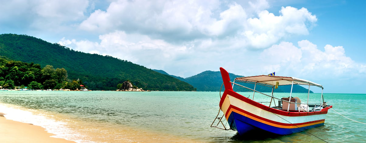Sunny beach and green mountains with colourful boat in Penang, Malaysia