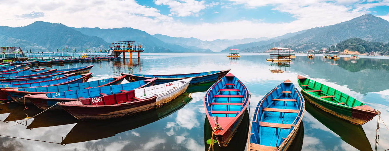 Colourful boats at shore of beautiful Phewa lake. Pokhara, Nepal with Annapurna range in background