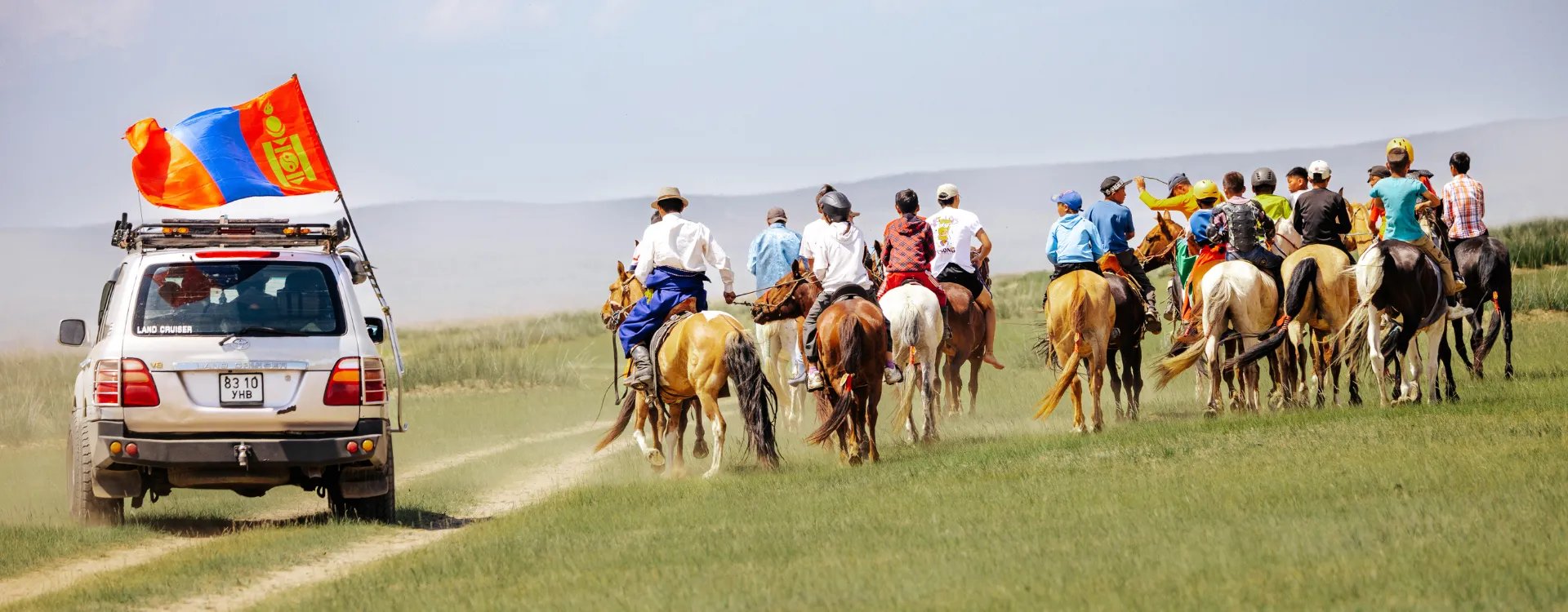 People on horseback and an SUV in the Mongolian steppe during the Naadam festival