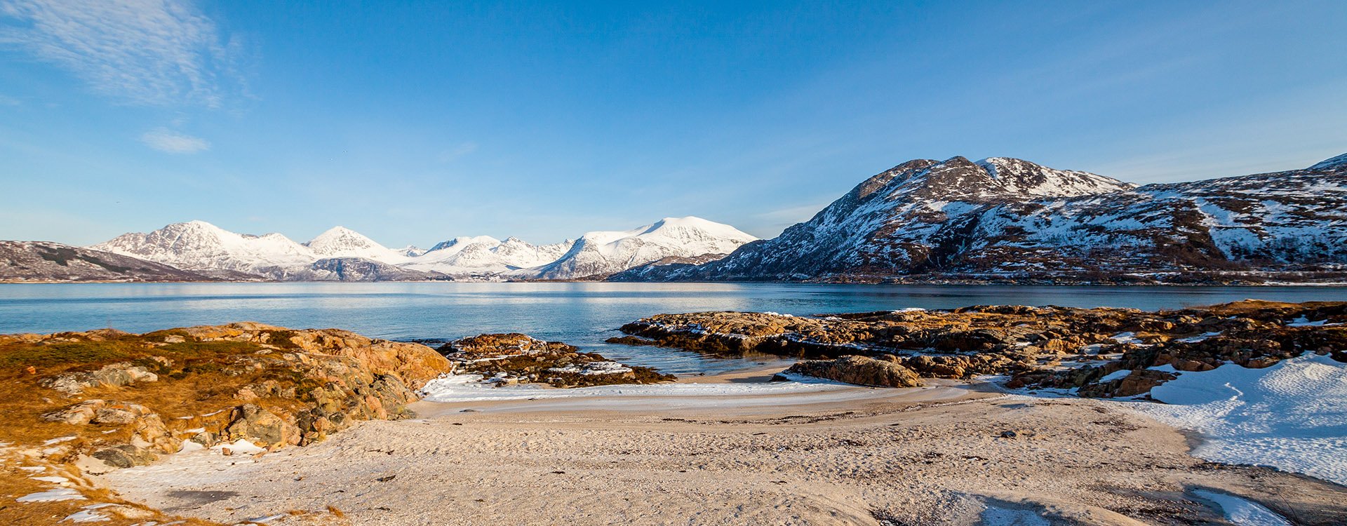 Snowy mountains and bright blue sky in the background. Spring landscape with melting snow and ice. Arctic Circle, Sommaroy, Norway