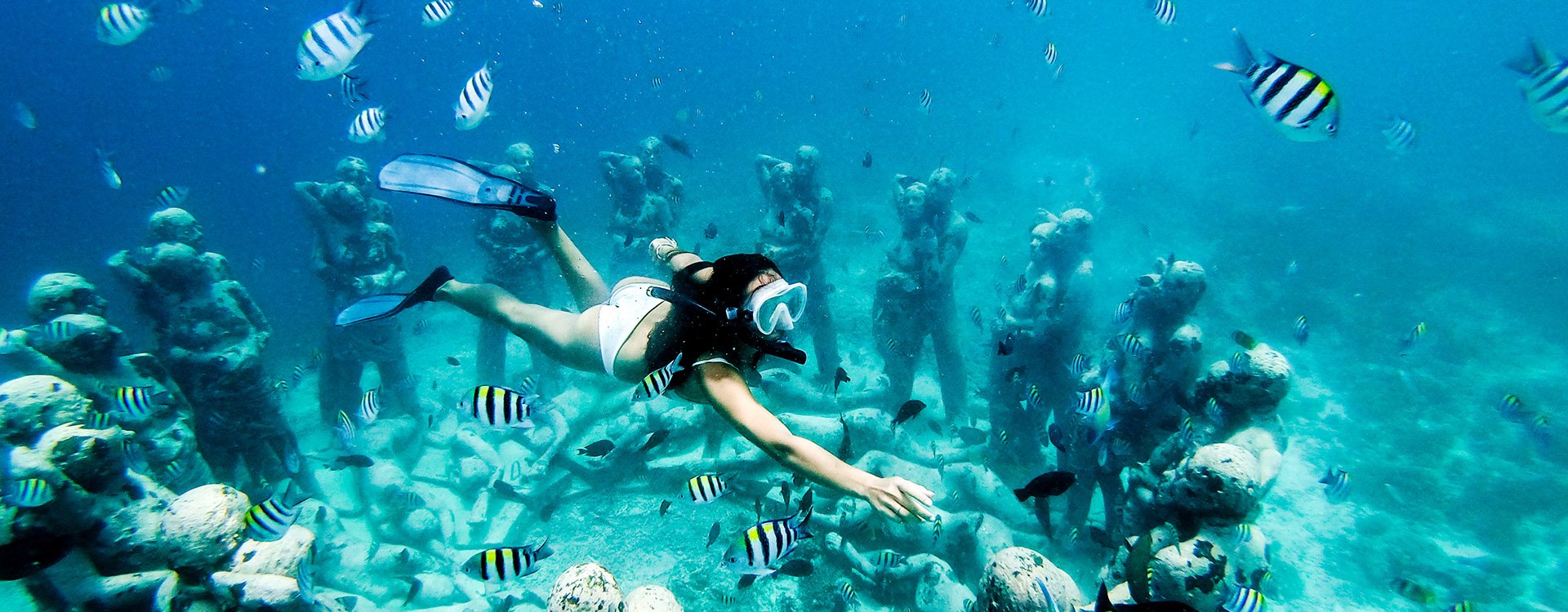 Snorkel woman swimming in a turquoise ocean under the flooded statues. Free diving.