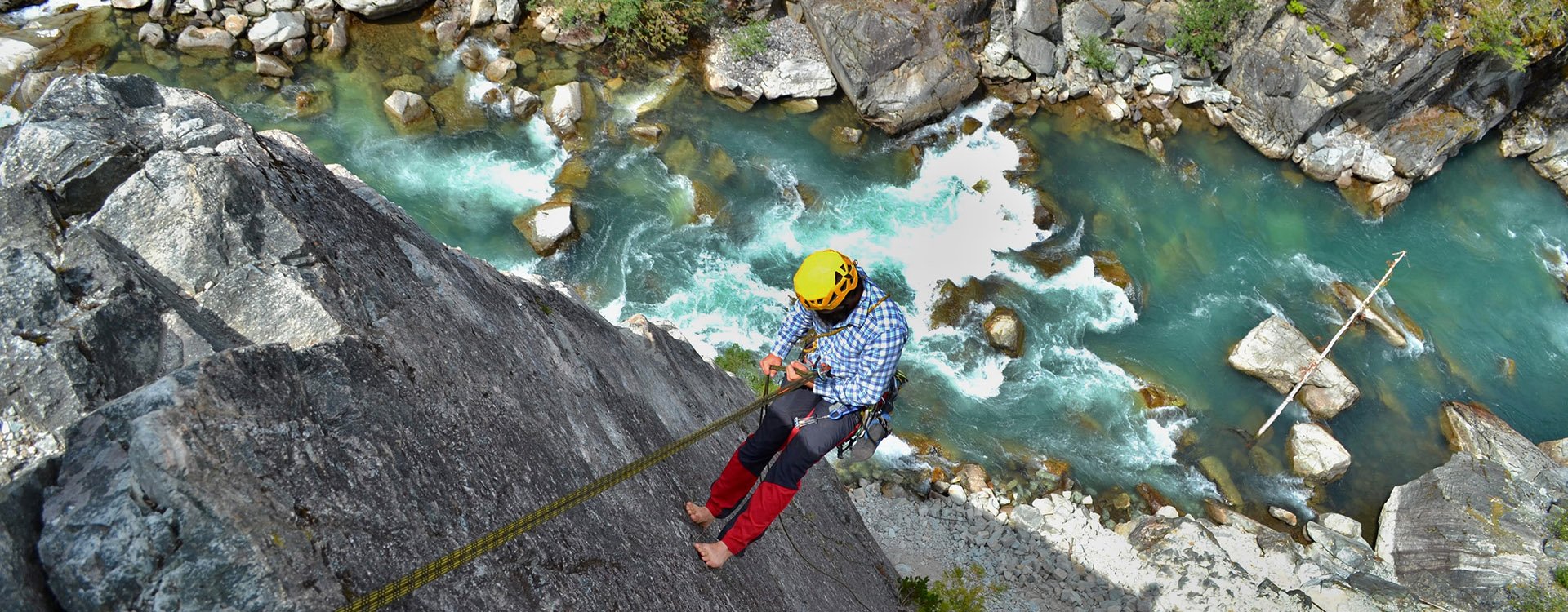 Climbing the majestic Star Chek multi-pitch route south of Whistler. Young man rappels beautiful climbing route above the wild river