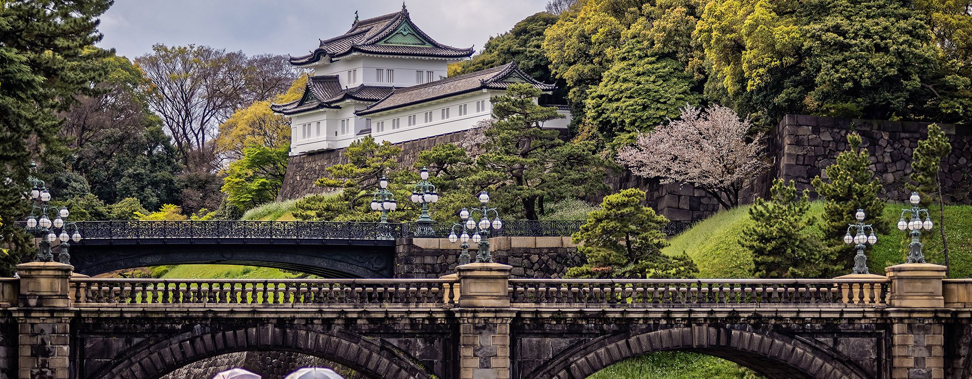 Two young ladies with umbrellas admire the striking Imperial Palace in Tokyo, Japan