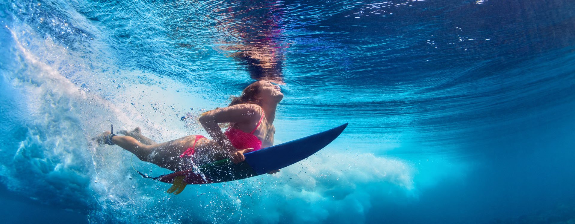 Girl in pink bikini surfing under waves