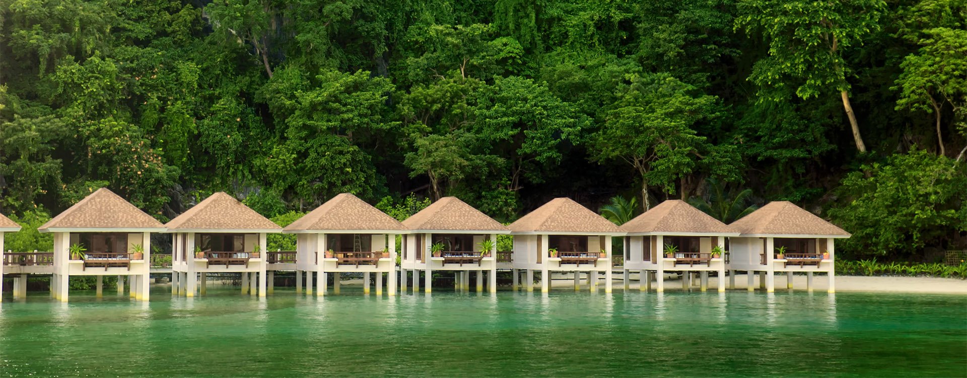 Cottages on stilts in El Nido, Palawan, Philippines, green rainforest background