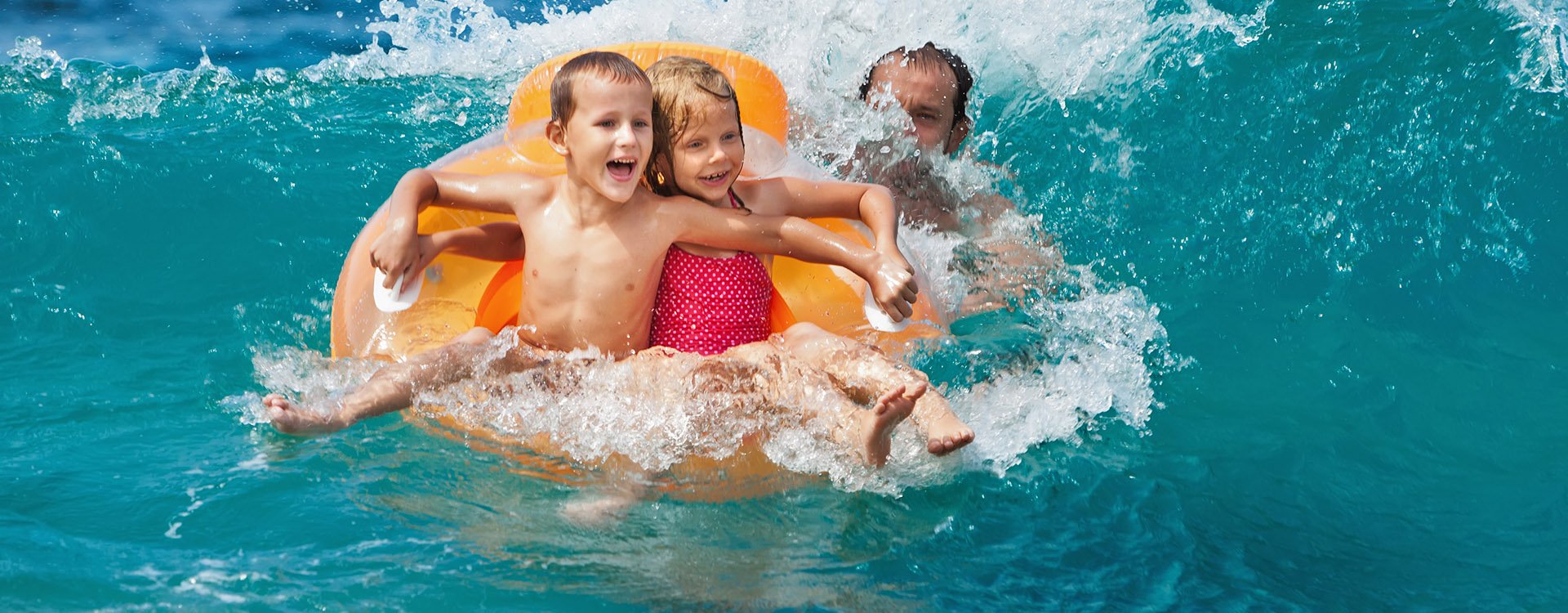 Happy kids have fun in sea surf on beach. Joyful couple of children on inflatable ring ride on breaking wave