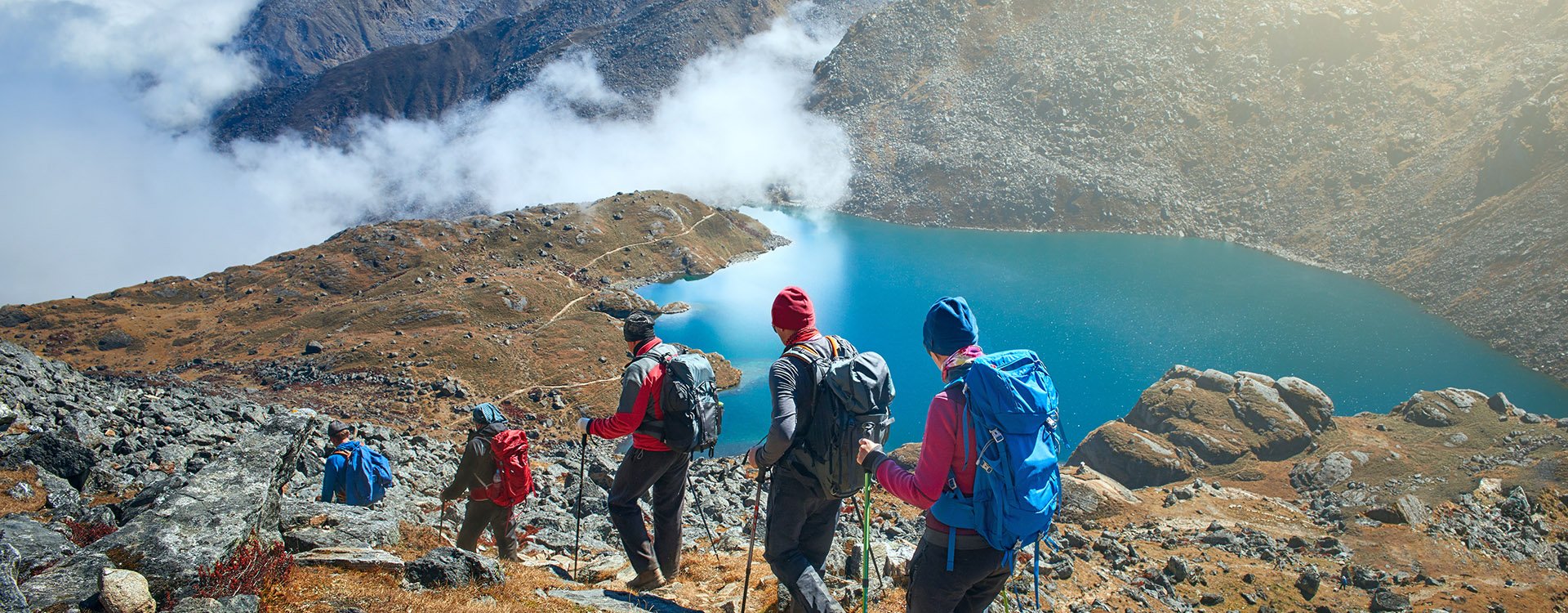 Group of tourists with backpacks descends down mountain trail to lake during hike in the national park Lantang, Nepal