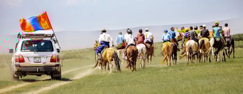 People on horseback and an SUV in the Mongolian steppe during the Naadam festival