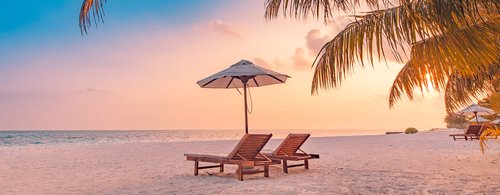 Summer beach landscape. Luxury vacation. Panoramic of sunset beach, two loungers umbrella, palm leaf, colorful sunset sky for paradise island view