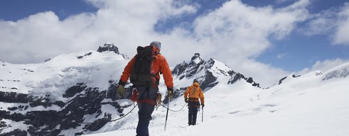 Rear view of two hikers joined by safety line in snowy mountains