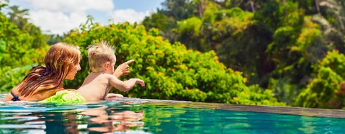 Family Bali beach holiday concept. Happy son with mother - active baby at poolside in infinity swimming pool