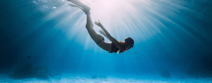 Young woman free diver glides over sandy sea with fins. Freediving in blue ocean